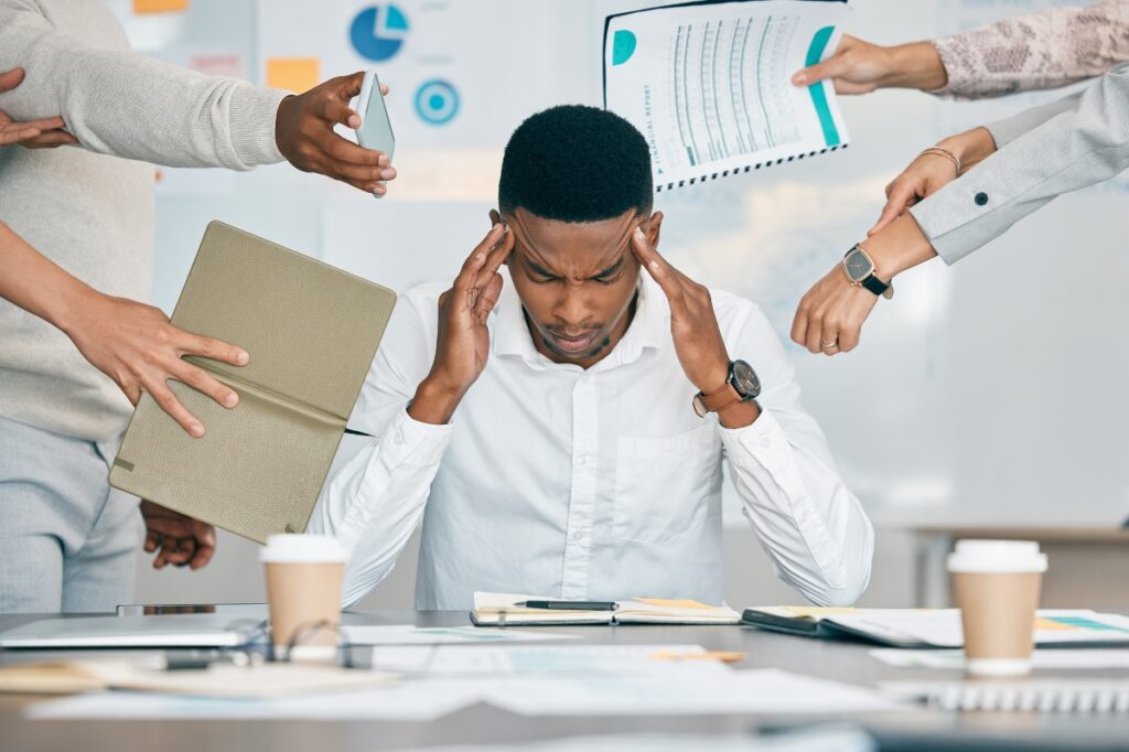 A person looking overwhelmed at a desk, surrounded by paperwork.