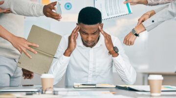 A person looking overwhelmed at a desk, surrounded by paperwork.