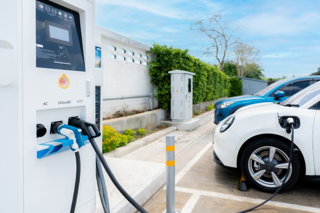 Progressive businesswoman insert charger plug from charging station to her electric vehicle with apartment condo building in background. Eco friendly rechargeable car powered by sustainable energy